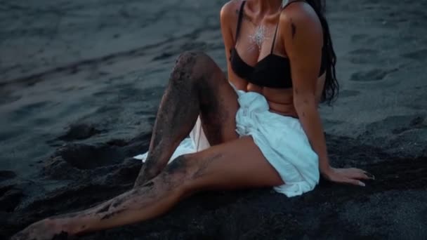 一个年轻美丽的欧洲黑发女孩坐在沙滩上化妆和身体的视频 — 图库视频影像