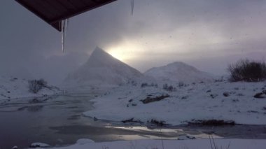 Kış Norveç. Lofoten. Dağlar, bulutlu ve kar yağışı gün batımında küçük bir nehir