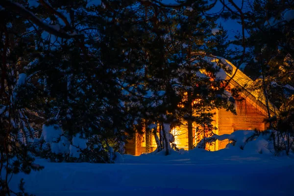 밤에 눈덮인 숲 속에 있는 조명을 받는 작은 집 — 스톡 사진