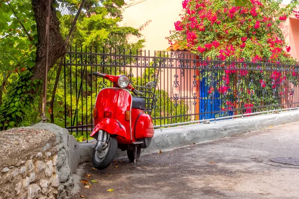 Scooter rosso al recinto di un giardino fiorito Foto Stock Royalty Free