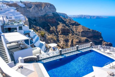 Yunanistan. Santorini. Thira Adası. Oia 'nın yüksek kıyısında bir villa. Güneşli havalarda dinlenmek için havuz ve güneş dinlenme yerleri. Deniz Burnu