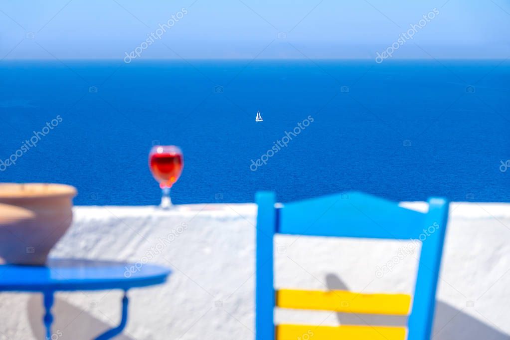 Defocused chair, table and glass of wine and a white sailing yacht far into the sea