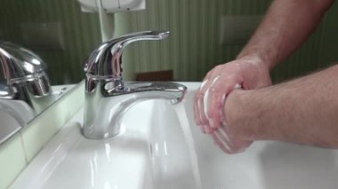 Tuvalette. Beyaz lavabo ve krom musluğu. Bir adam ellerini sabunla yıkar. Yavaş çekim