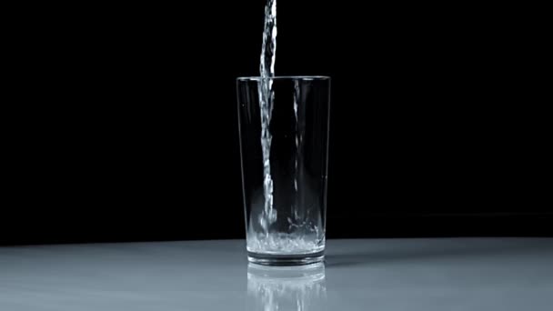 Glazen Beker Een Zwarte Achtergrond Water Giet Met Spatten Langzame — Stockvideo
