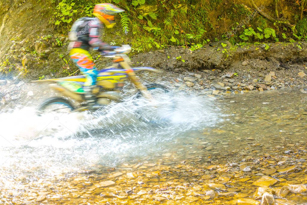 Sunny summer day. Enduro athlete overcomes a forest stream. A lot of water spray