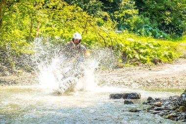 Ormanda güneşli bir yaz günü. Enduro sporcusu sığ bir dereyi su sıçramalarıyla aşıyor.