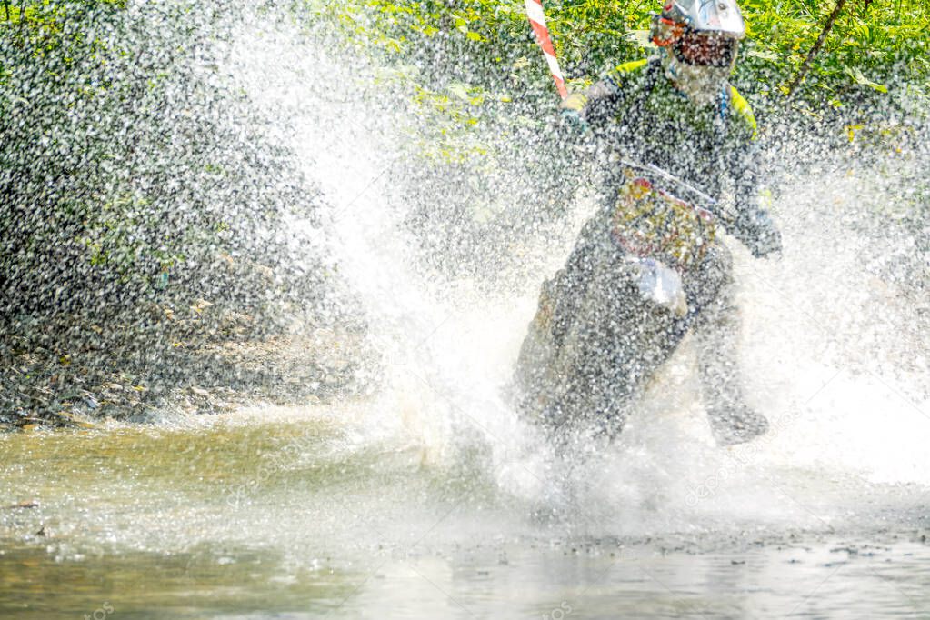 Summer sunny day in the forest. Enduro athlete overcomes a shallow stream with lots of splashes