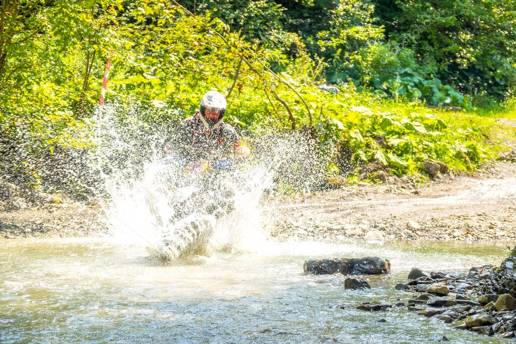 Summer sunny day in the forest. Enduro athlete overcomes a shallow stream with lots of water splashes