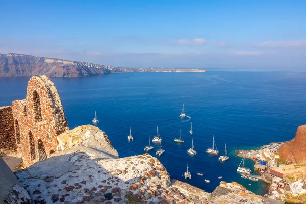 Yunanistan. Santorini. Thira Adası. Oia 'daki harabeler ve limandaki yelkenli katamaranların manzarası.