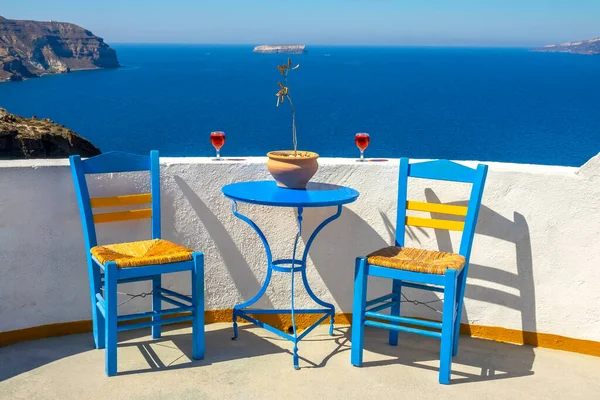 Yunanistan. Santorini. Thira Adası. Oia 'daki bir kafeden güneşli bir deniz manzarası. İki sandalye ve iki kadeh şarap.