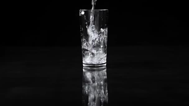 Gobelet de verre. L'eau coule avec éclaboussures sur un fond noir. Mouvement lent 