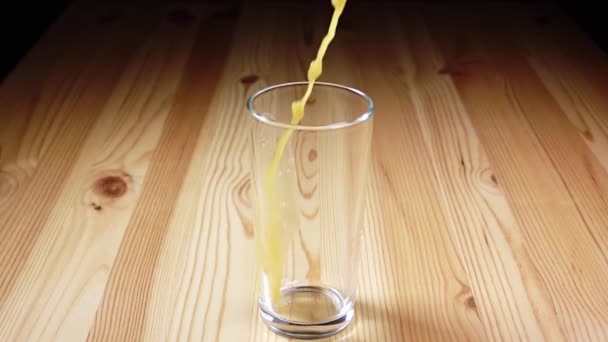 グラスカップは木製のテーブルの上に立っている スプレーでオレンジジュースのストリーム スローモーション — ストック動画