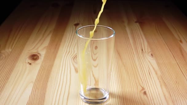 Coupe en verre se tient sur une table en bois. Un jet de jus d'orange avec spray. Mouvement lent 