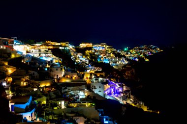 Yunanistan. Santorini 'nin üzerinde karanlık bir gece. Oia 'da evler, havuzlar ve restoranlar aydınlatılıyor