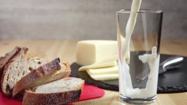 Süt akıntısı bir bardağa dökülür. Yakınlarda bir kaç dilim taze peynir ve ekmek var. Yavaş çekim