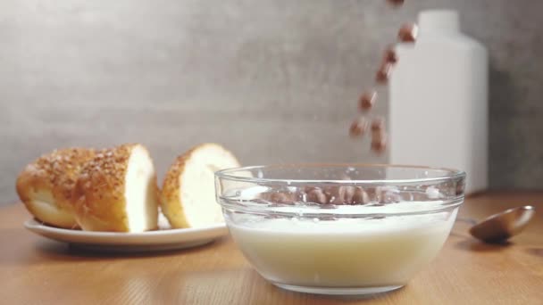 木製のテーブルの上で朝食 ソーサーの上に新鮮なパン ミルクのボウルに落ちるチョコレートコーンフレーク スローモーション — ストック動画
