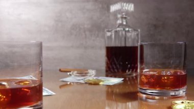 Buzlu viski ve parayla dolu bir hayat. Bir şişe viski ve arkasında puro olan bir kül tablası. Masaya bir deste iskambil kağıdı düşüyor. Yavaş çekim