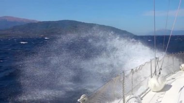 Güneşli ve rüzgarlı bir gün. Beyaz yelkenli yat dalgalarda yüzer ve bir su püskürtme bulutu yaratır. Yavaş çekim