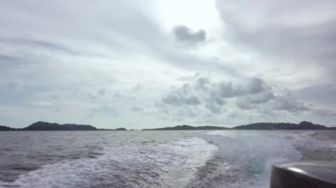 Tropik adalar arasında sakin su yüzeyi. Bulutlu. Sürat teknesinin arkasında iz bırakma