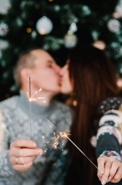Sevgi dolu bir çiftin arka planında havai fişekler. Bir adam ve bir kadın yılbaşı ağacının yanında kıvılcım saçıyor. Mutlu Noeller ve mutlu tatiller! Xmas.