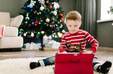 Noel Baba süveteri giyen mutlu çocuk tablete bakar ve oynar, Gadge.