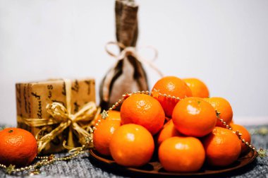 Tabakta mandalina, hediye kutusu, kar taneleri ve gri örülmüş arka planda kırsal stil çuvalı.
