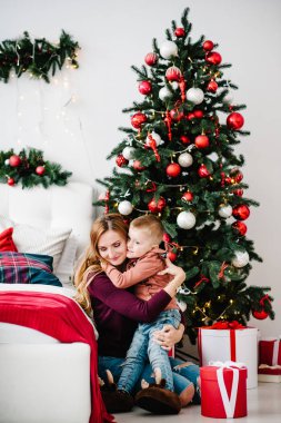 Anne oğluna Noel ağacının yanında bir hediyeyle sarıldı. Mutlu yıllar ve mutlu Noeller. Noel dekore edilmiş iç mekan. Aile tatili kavramı. Kapat..