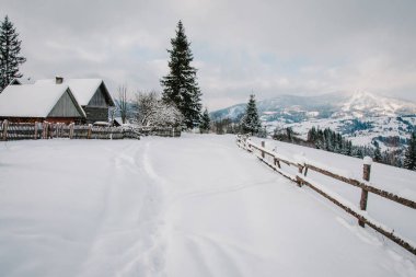 Snow-capped wooden fence, houses in mountains Carpathians Ukraine clipart