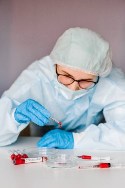 Coronavirus. Doktor, hemşire, koruyucu kıyafetli bilim adamı ve maske takmış bir tüpü biyolojik numuneyle test ediyor. Corona virüsü ile kirlenmiş bir şırınga. Laboratuar testi - Pozitif sonuç.
