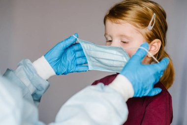 Coronavirus. Hemşire, koruyucu kıyafetli doktor çocuk için tıbbi maske takıyor. Covid-19 enfeksiyonuna karşı önleyici önlemler. Gribe karşı korunma kavramı, korona virüsü salgını.