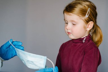 Coronavirus. Hemşire, koruyucu kıyafetli doktor çocuk için tıbbi maske takıyor. Covid-19 enfeksiyonuna karşı önleyici önlemler. Gribe karşı korunma kavramı, korona virüsü salgını.