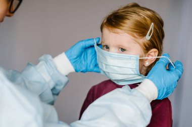 Coronavirus. Hemşire, koruyucu giysili doktor, çocuk için yüzünde tıbbi maske var. Covid-19 enfeksiyonuna karşı önleyici önlemler. Gribe karşı korunma kavramı, korona virüsü salgını.
