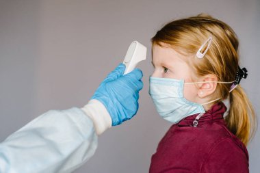 Coronavirus. Hemşire ya da doktor, virüs salgını konsepti için kızıl ötesi alın termometresi (silah) kullanarak kızın vücut ısısını kontrol eder. Yüksek sıcaklık.
