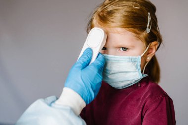 Coronavirus. Hemşire ya da doktor, virüs salgını konsepti için kızıl ötesi alın termometresi (silah) kullanarak kızın vücut ısısını kontrol eder. Yüksek sıcaklık.
