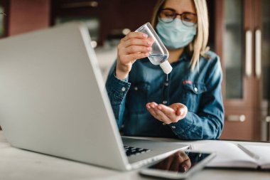 Coronavirus. Dezenfekte jeli. İş kadını karantinada koruyucu maske takıyor. Mikropları yok etmek için bakteriyel jel temizliyorum. Evde kal. Kız öğreniyor, dizüstü bilgisayar kullanarak. Bağımsız.