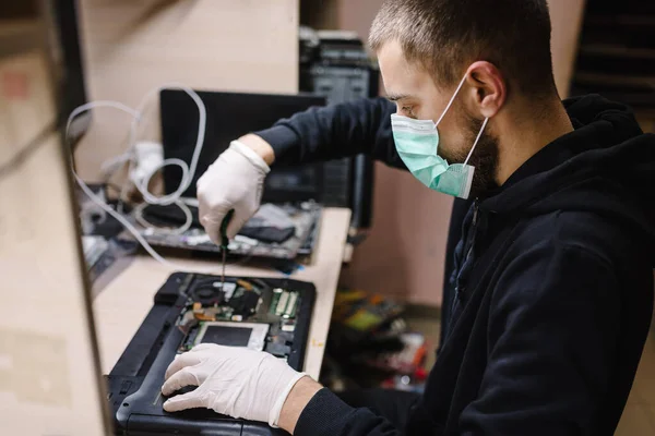 Laboratuvarda dizüstü bilgisayarı tamir eden bir teknisyen. Onarım bilgisayarı, elektronik, güncelleme, teknoloji kavramı. Coronavirus. Atölyede çalışan, koruyucu maske takan bir adam..