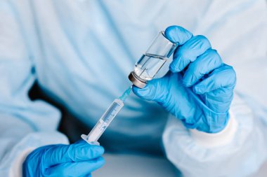 Biyolojik tehlike. Çin koronavirüsü salgını. Doktor, hemşire, koruyucu kıyafetli ve maskeli bilim adamı şırınga ve aşı tutuyor. Grip aşısı, koronavirüs, ebola, tüberküloz.