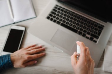 Coronavirus. Dezenfektan. Karantinada çalışan bir iş kadını. Mikropların antibakteriyel spreyini yok etmek için cep telefonu ve dizüstü bilgisayar temizliyorum. Evde kal. Covid-19 virüsünü engelle