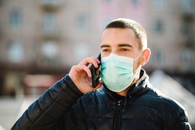 Coronavirus. Tıbbi koruyucu maske takan, cep telefonuyla konuşan, sokakta yürüyen bir adam. Covid-19 'u, gribi önle. Virüs, salgın hastalık, panik konsepti.
