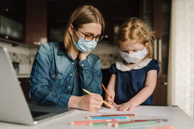 Coronavirus. Karantinada anne ve kızı koruyucu maske takıyor. Evde kalıp bebeğe bakarken dizüstü bilgisayarda çalışan bir kadın. Serbest bir iş. Çocuk gürültü yapıyor, oynuyor ve anneyi rahatsız ediyor..
