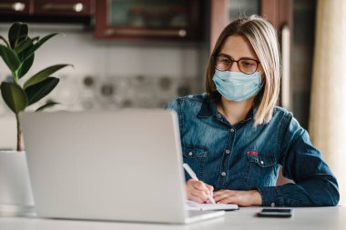 Coronavirus. Karantinada koruyucu maske takan bir iş kadını. Evde kal. Kız ev bilgisayarını kullanarak öğreniyor. Serbest çalışıyorum. İletişim ve teknoloji kavramı.