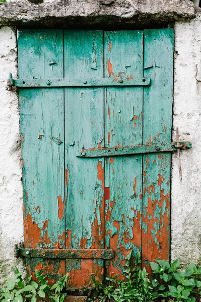 Old green wooden door in a white wall. Barn. Cracked. The door to the hinges. Peeling red paint. Basement.