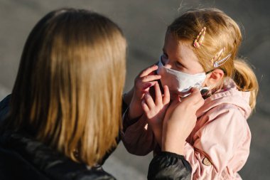 Coronavirus son konsept. Artık Coperid-19 yok. Küçük kız, anne sokakta yürürken maske takıyor. Anne, maske takan mutlu çocuğu çıkarır. Dışarıda çocuklu bir aile. Başarıyı kutlamak. Salgın sona erdi..