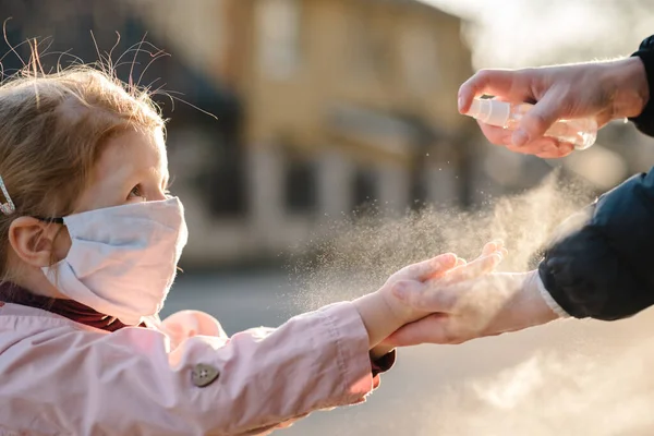 Coronavirus. Kadın, sokakta koruyucu maske takmış bir çocuğa sprey dezenfektan sıkar. Covid-19 enfeksiyonuna karşı önleyici önlemler. Anti bakteriyel yıkama spreyi. Hastalık koruması.