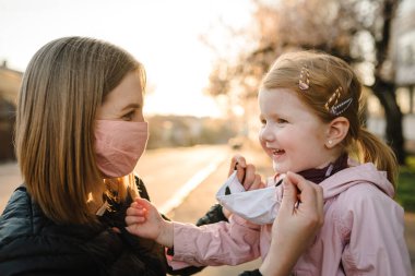Coronavirus son konsept. Artık Coperid-19 yok. Küçük kız, anne sokakta yürürken maske takıyor. Anne, maske takan mutlu çocuğu çıkarır. Dışarıda çocuklu bir aile. Başarıyı kutlamak. Salgın sona erdi..