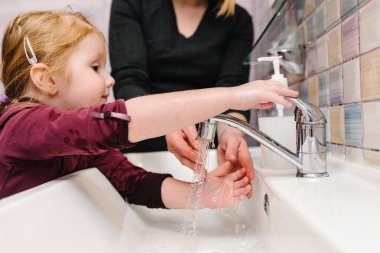 El yıkama. Koronavirüsü yaymayı bırak. Covid-19 enfeksiyonuna karşı önleyici önlemler. Anne çocuğa ellerini antibakteriyel sabunla, sıcak suyla ovalayarak ve parmaklarıyla nasıl yıkayacağını söyler..
