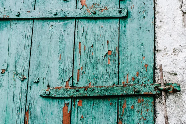 Part old green wooden door in a white wall. Barn. Cracked. The door to the hinges. Peeling red paint. Closed of wood.