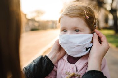 Coronavirus son konsept. Artık Coperid-19 yok. Küçük kız, anne sokakta yürürken maske takıyor. Anne, maske takan mutlu çocuğu çıkarır. Dışarıda çocuklu bir aile. Başarıyı kutlamak. Salgın sona erdi..