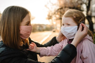 Coronavirus son konsept. Artık Coperid-19 yok. Küçük kız, anne sokakta yürürken maske takıyor. Anne, maske takan mutlu çocuğu çıkarır. Dışarıda çocuklu bir aile. Başarıyı kutlamak. Salgın sona erdi..