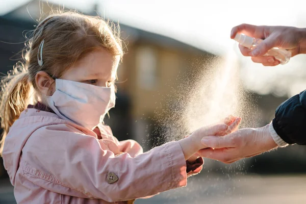 Coronavirus. Woman use spray sanitizer on hands child  in a protective mask on the street. Preventive measures against Covid-19 infection. Antibacterial hand-washing spray. Illness protection.